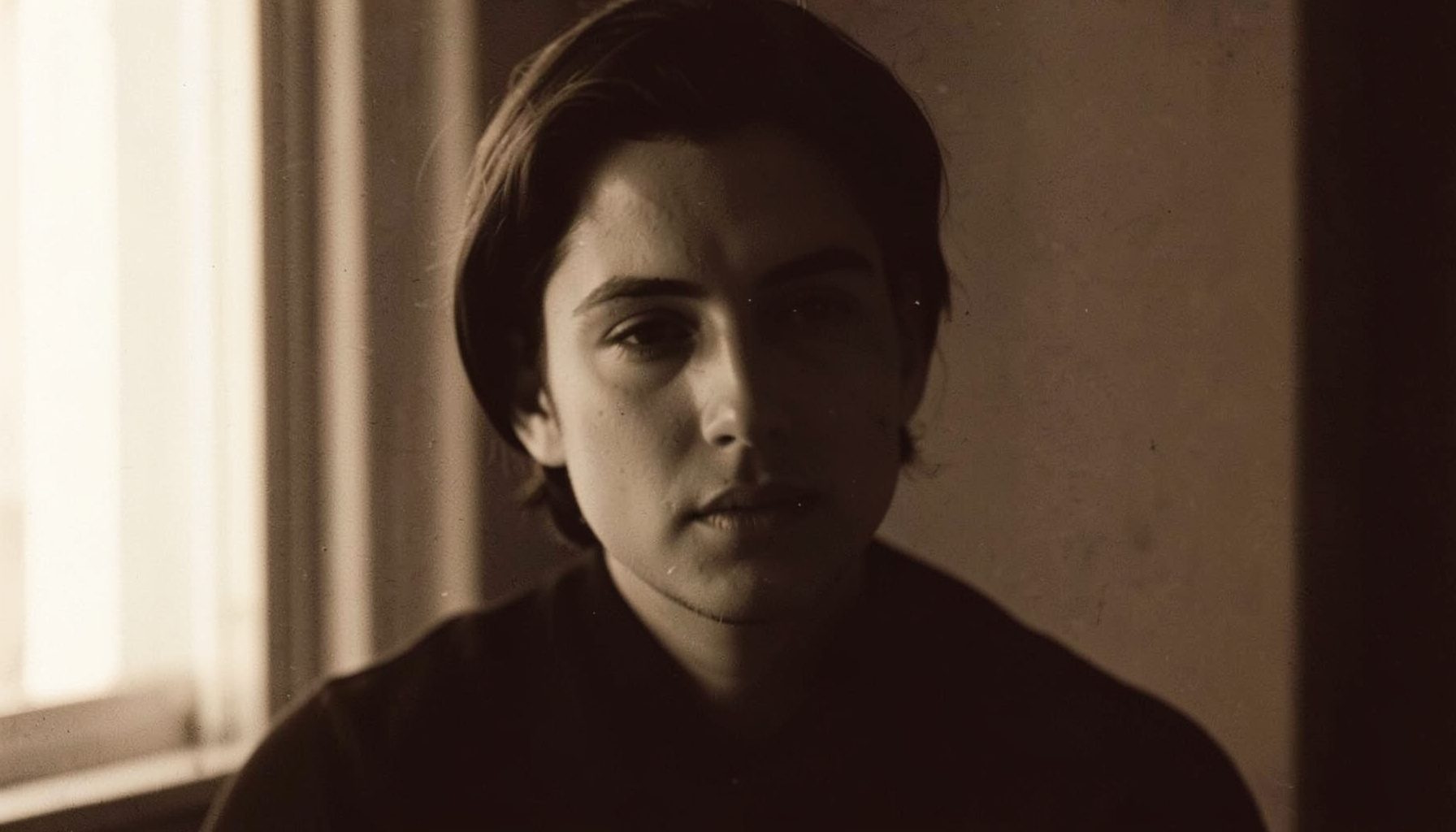 Duotone portrait of a person in soft window light, warm sepia and deep brown tones, quiet and contemplative mood