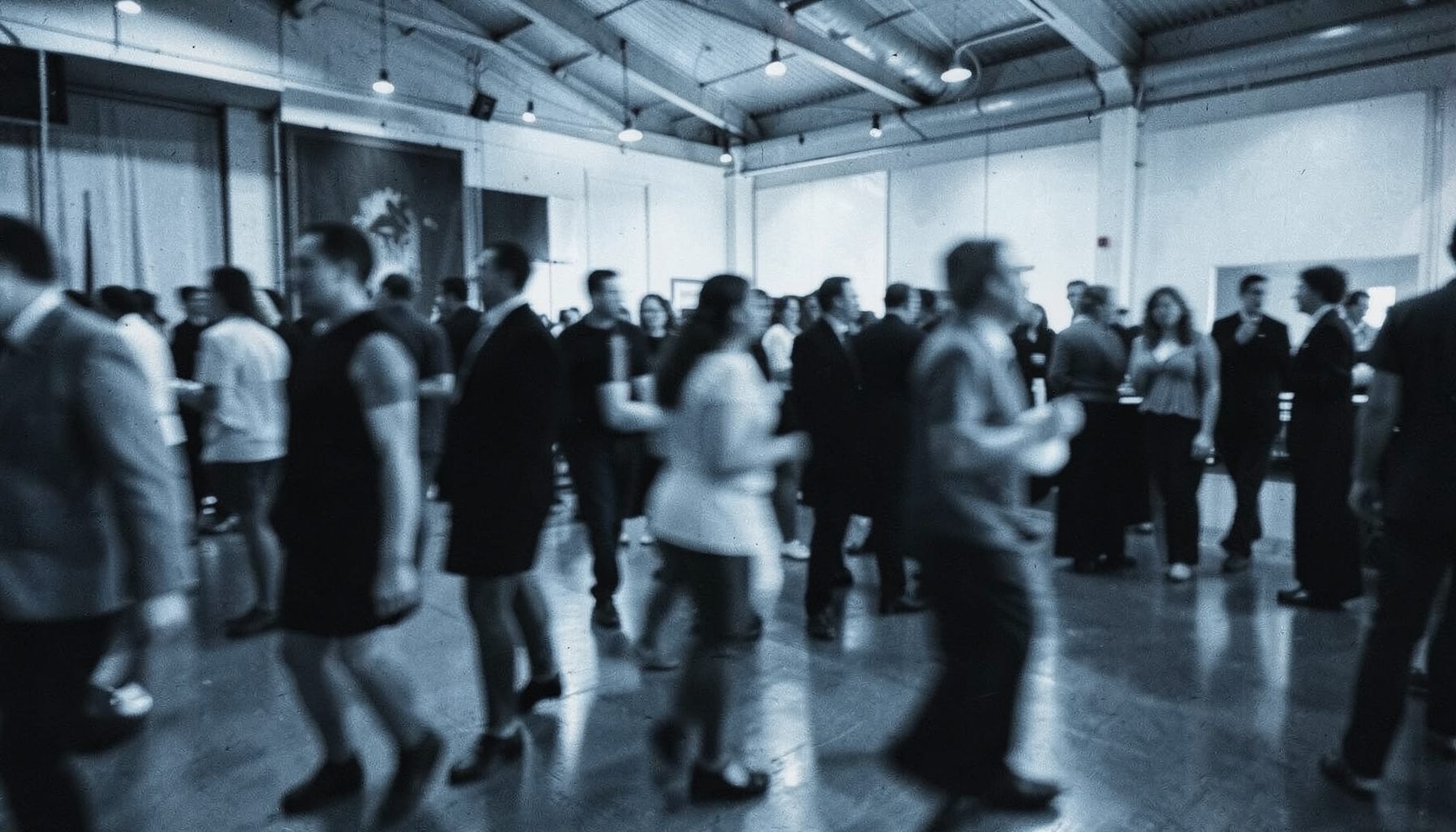 Duotone scene of a busy event hall with blurred figures in motion, cool steel blue and charcoal, candid reportage feel