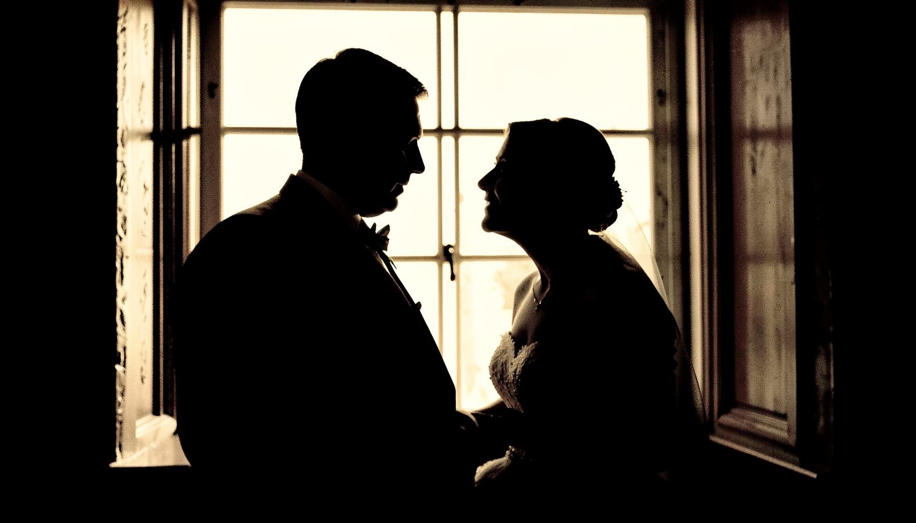 Duotone wedding moment — a couple in silhouette against a bright window, rich black and warm ivory tones