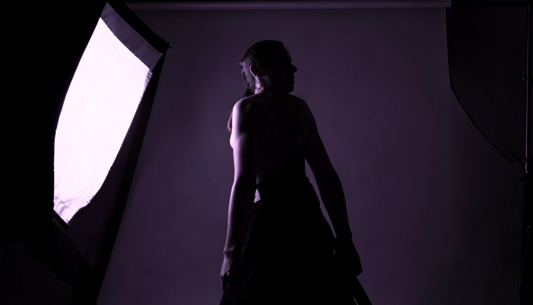 Duotone studio setup with softbox and backdrop, a figure in dramatic side lighting, deep violet and charcoal tones