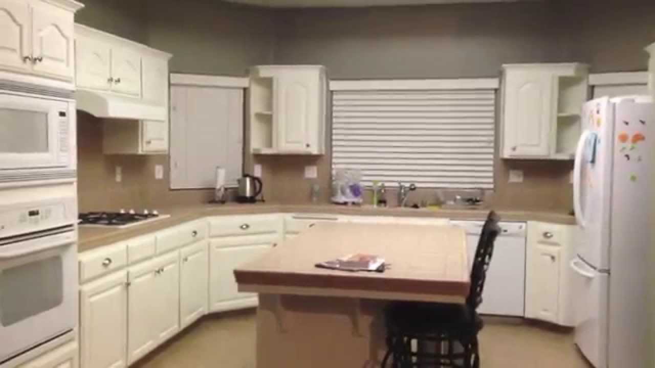Interior of a kitchen with white cabinetry, tan countertops, built-in appliances, and a central island with a stool, dim warm lighting